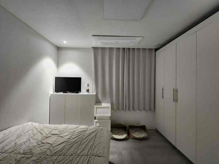 白とグレーのモノトーンの寝室、ベッドとテレビ台、収納キャビネットが整然と配置された落ち着いた空間
