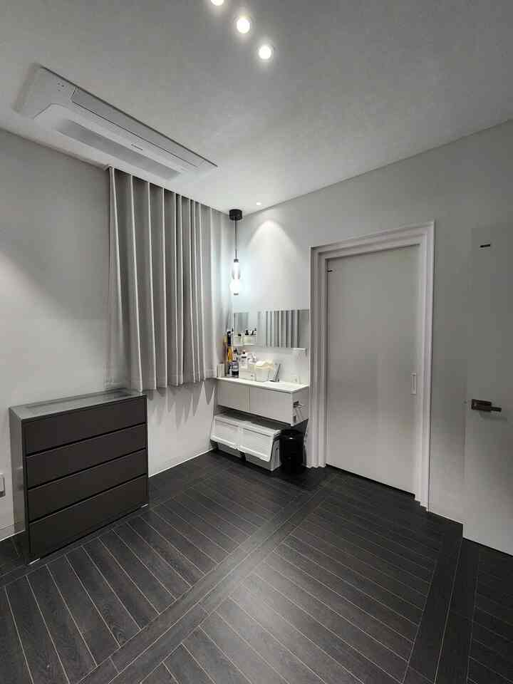 白い壁とダークブラウンの床のウォークインクローゼット、シンプルモダンな収納家具と照明が配置された清潔感のある空間