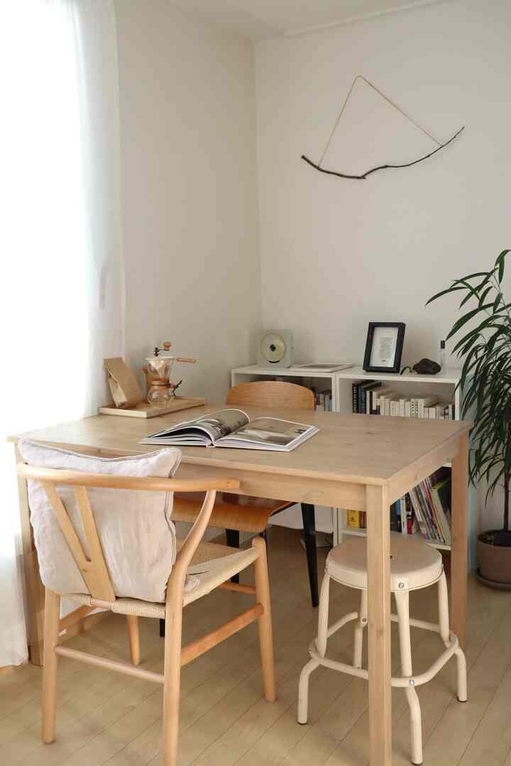 ナチュラルな色調のダイニング、木製のダイニングテーブルとさまざまなデザインのチェア、アイボリースツールが配置された雰囲気のある空間