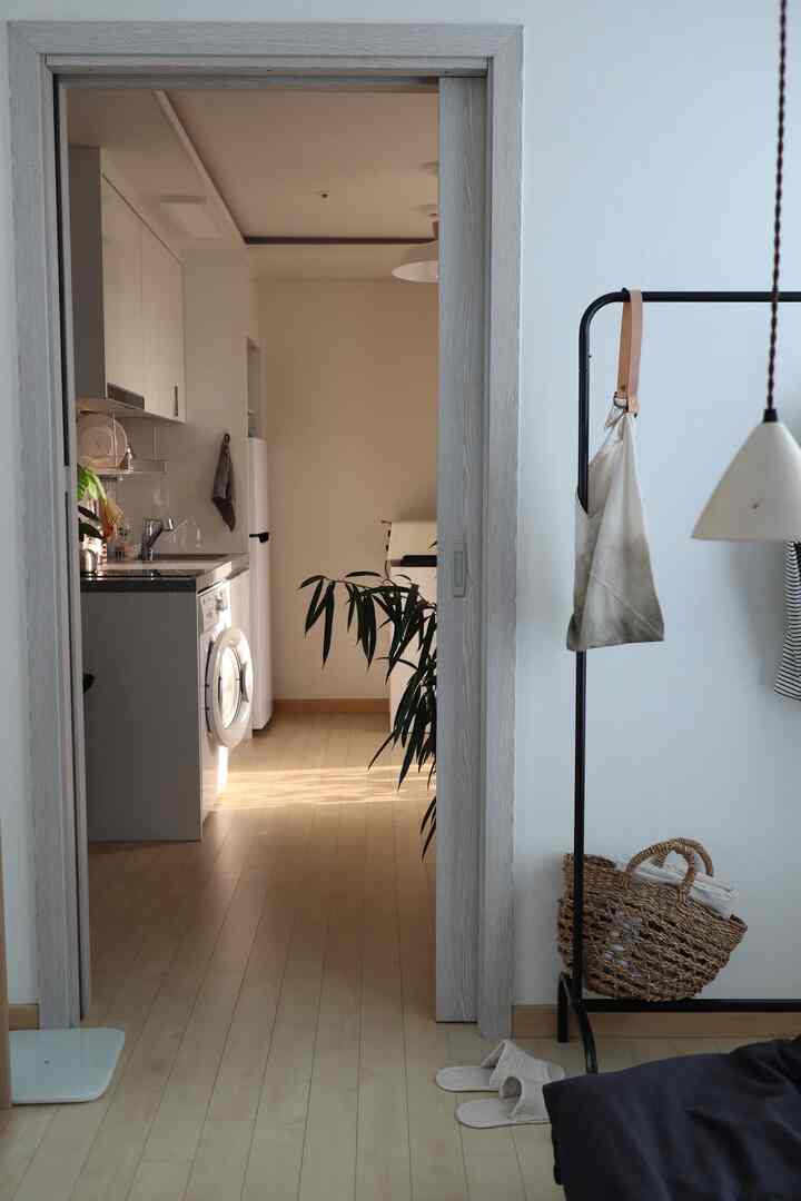 ナチュラルな色調の寝室から開けた引き戸越しに見えるすっきりとしたキッチンと調和のとれたフロアのインテリア