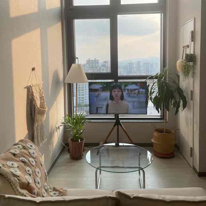 アイボリーと木目調が調和する居心地の良いリビング、透明なテーブルと豊かな植物が空間を彩る