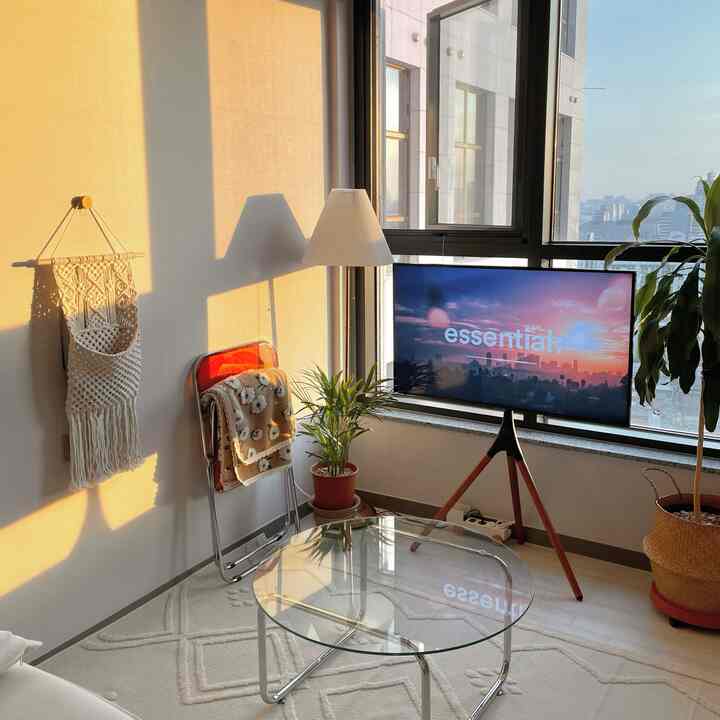 ベージュとホワイトの色調のリビング、透明なガラスのコーヒーテーブルと植物、テレビスタンドが配置された温かみのある雰囲気のインテリア