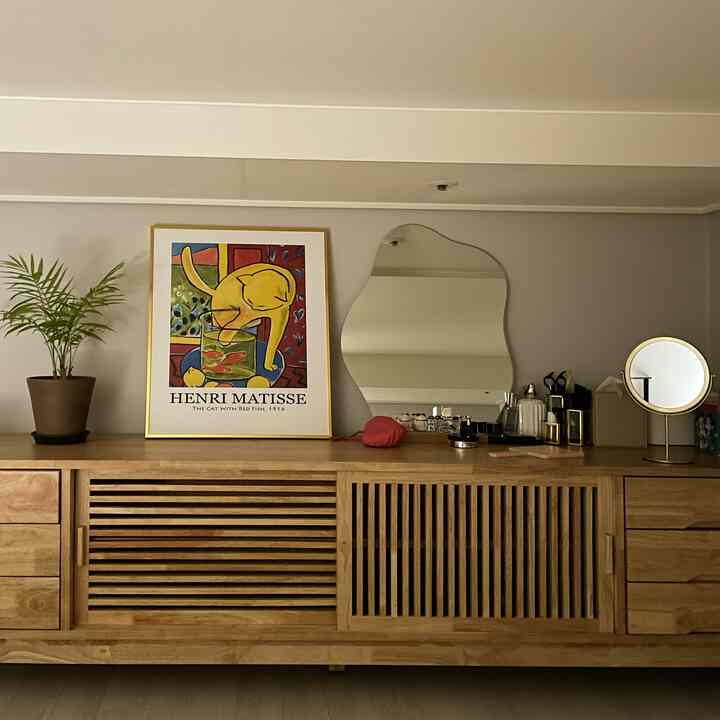 木目調とゴールドが調和したリビング、木製テレビ台とゴールドの額縁、鏡、植物が配置された雰囲気のあるインテリア