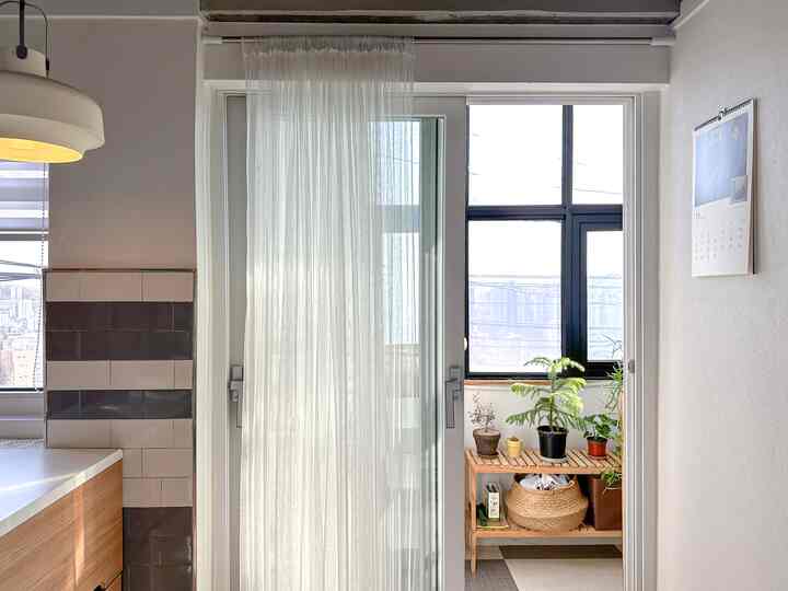 白とナチュラルカラーのバルコニー、木製の棚に植物が並び、薄いカーテンがかかる落ち着いた雰囲気のある空間