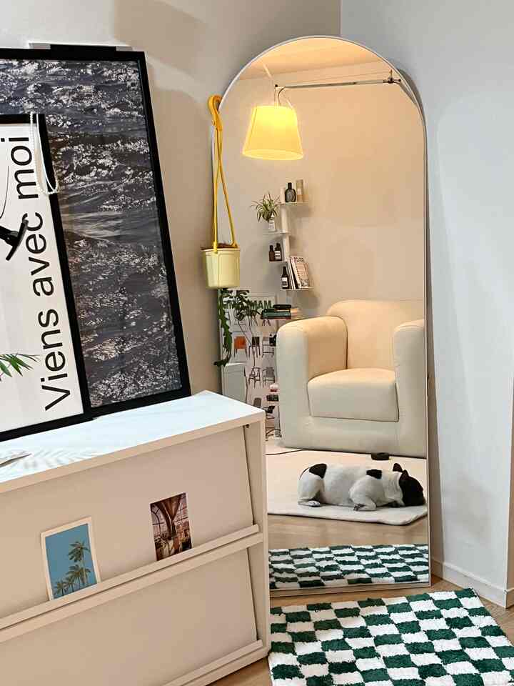 アイボリーとホワイト調の寝室、アーチ型の全身鏡とアームチェア、チェック柄のラグとペットの犬がいる雰囲気のあるインテリア