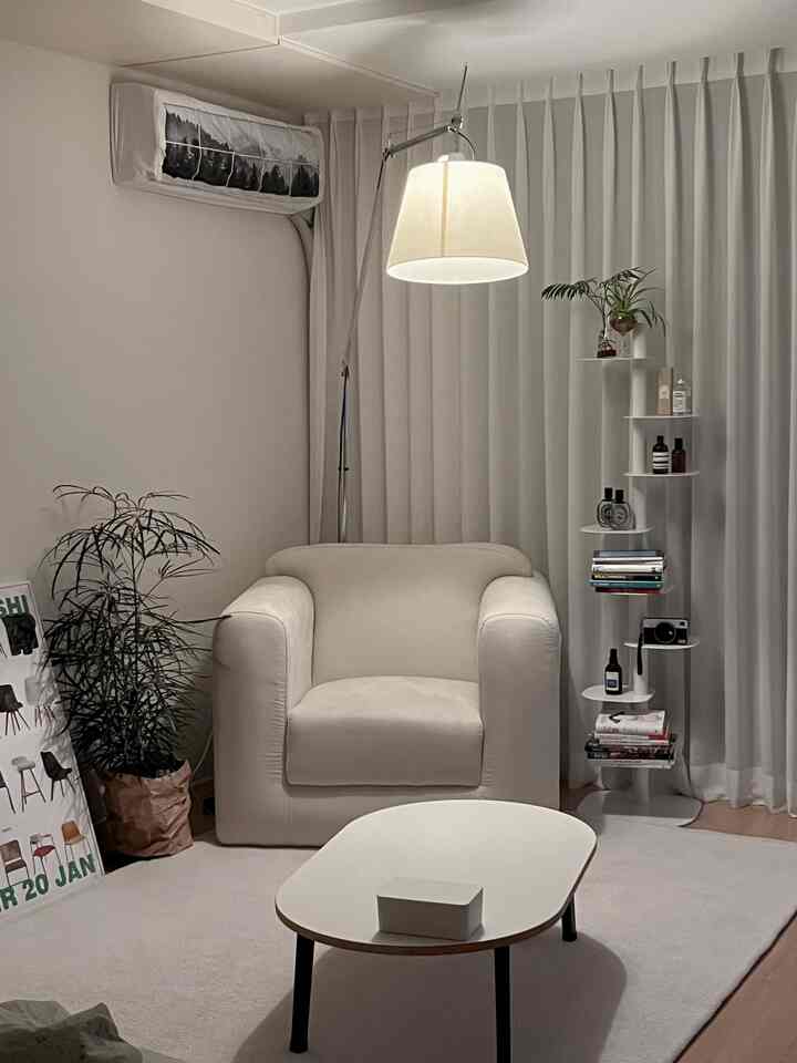 ナチュラルカラーのワンルームリビング、ベージュのアームチェアとホワイトのコーヒーテーブル、フロアランプが配置された落ち着いた印象の空間