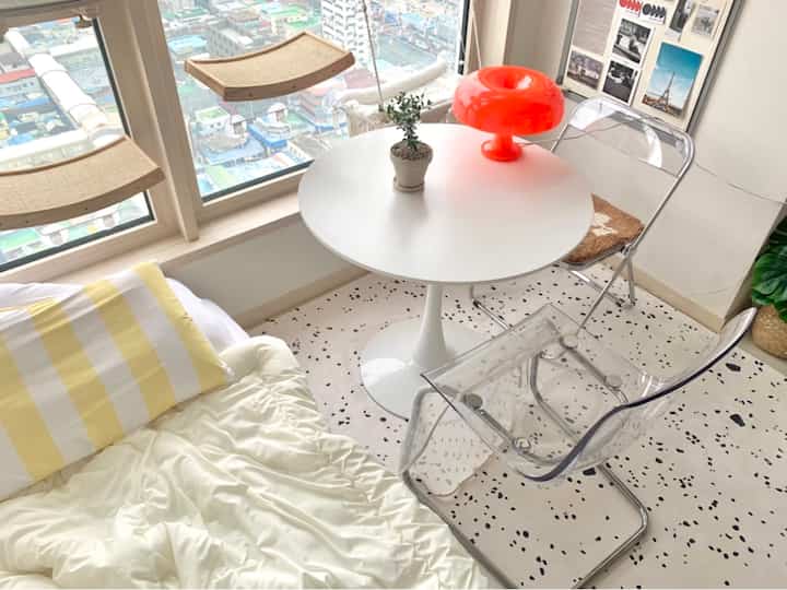 白を基調とした狭い部屋、円形テーブルと透明な椅子、オレンジ色のキノコ型ランプが配置された雰囲気のあるおうちカフェ