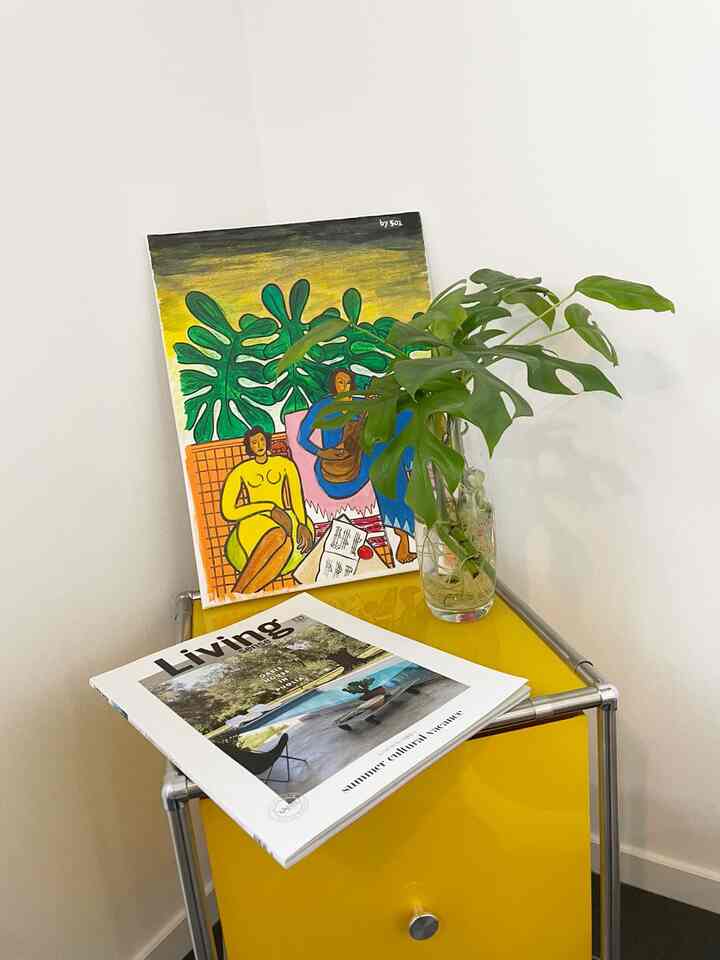 黄色のチェストの上に緑のモンステラとモダンアートが置かれたミニマルなリビングコーナー