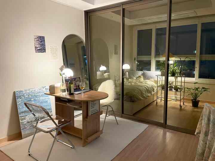 アイボリーとベージュのトーンのリビング、アーチ型全身鏡と半円テーブル、透明な椅子と植物が配置された雰囲気のある空間