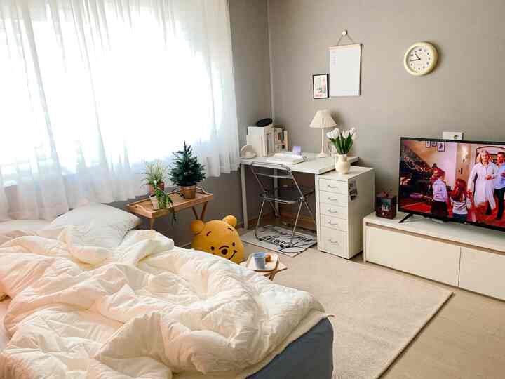 白とベージュのトーンの6畳寝室、デスクとテレビ台が配置されたシンプルな一人暮らしの空間