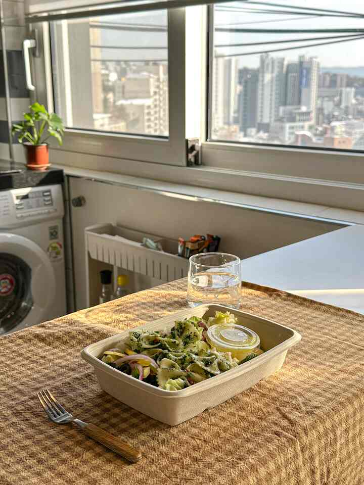 ベージュのテーブルクロスが掛けられたキッチンの食卓、簡単な食事が用意された落ち着いた一人暮らしの空間