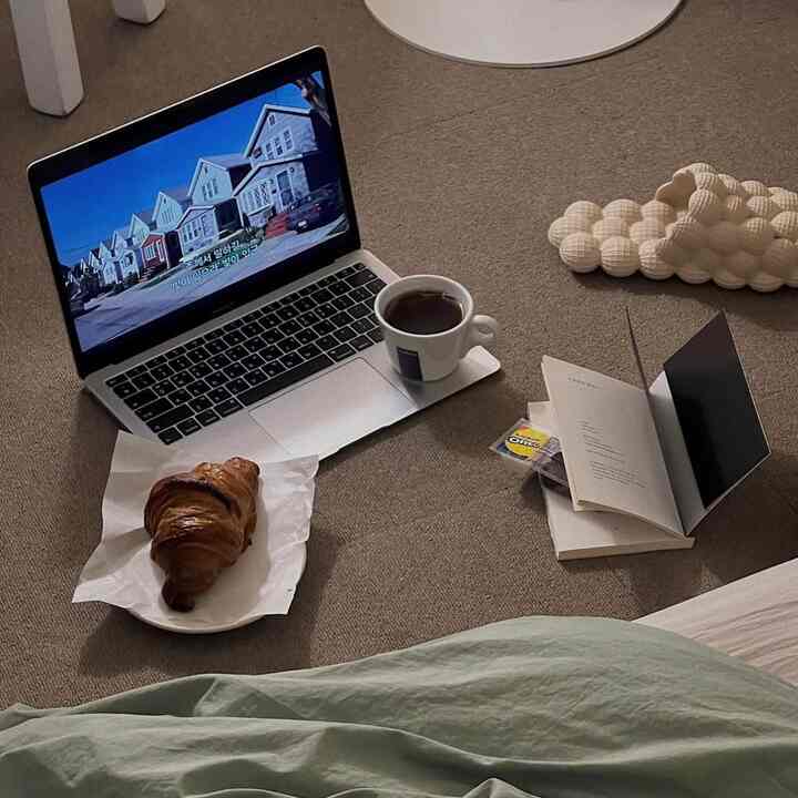 ベージュのカーペットの上にノートパソコンとコーヒーカップが置かれた、温かみのあるワンルームのホームカフェ風在宅勤務スペース