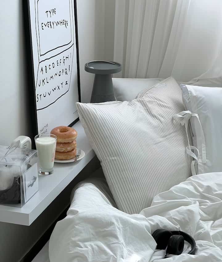 白とグレーのトーンの寝室、棚の上に枕とおやつがきれいに置かれた居心地の良い空間