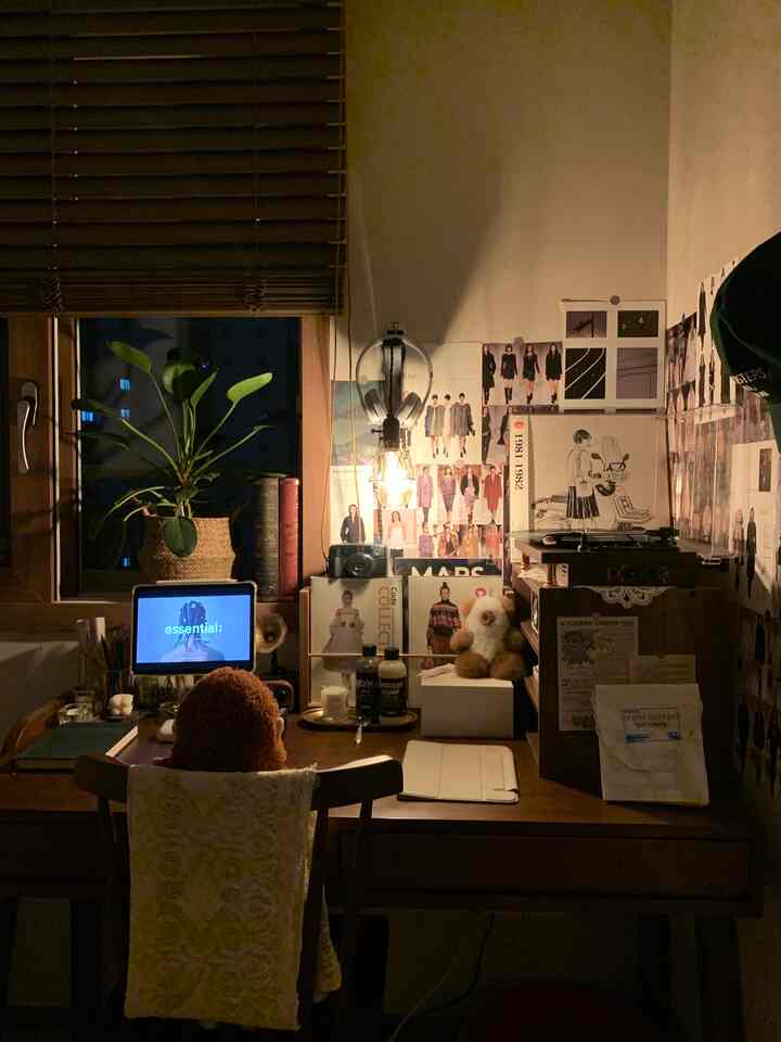 柔らかいライトブラウンのトーンがあるワンルームの作業スペース、ヴィンテージの小物と壁照明が調和した雰囲気あるインテリア