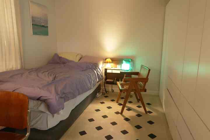 落ち着いた紫色の掛け布団とヴィンテージのナイトテーブルがある狭いワンルーム寝室の雰囲気のあるインテリア