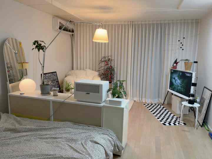 ホワイトとナチュラルトーンの寝室兼リビング、ソファとラグが配置された雰囲気のある空間