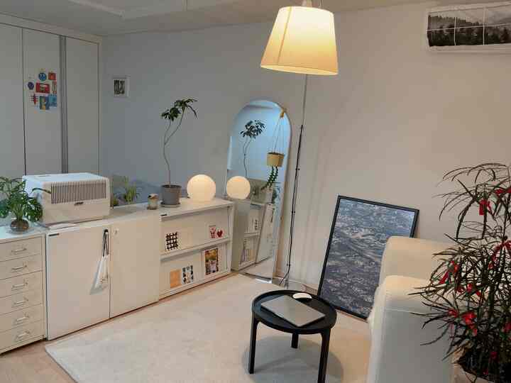 明るいホワイトと木目調の調和がとれたリビング、ソファとフロアランプ、ミニマルな収納が配置された落ち着いた空間