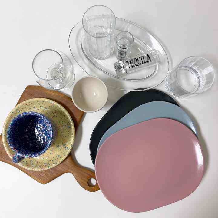 透明なグラスとピンク、青、黒の皿、木製のまな板が並べられた清潔感のあるテーブルの写真