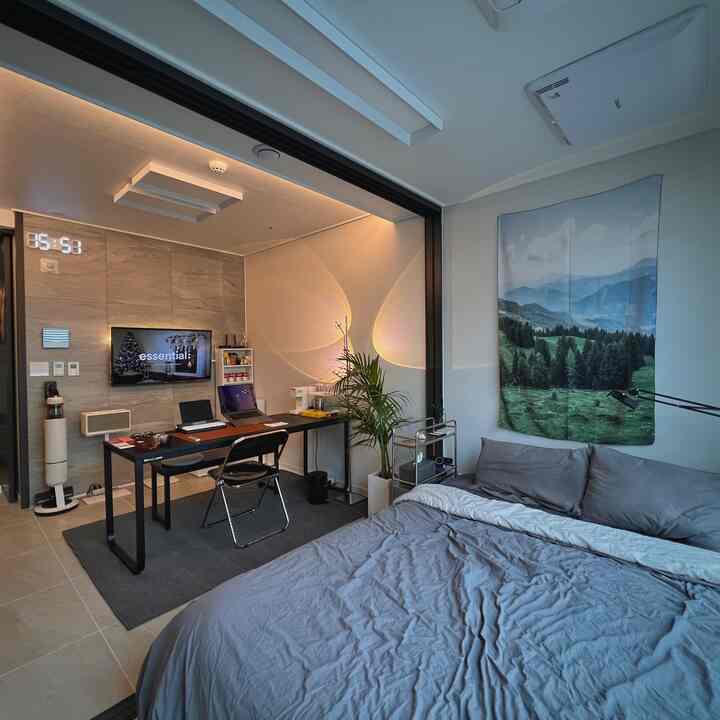 チャコール色調の寝室、低いベッドフレームと布製ポスター、モダンなホームオフィスデスクが配置された雰囲気のあるインテリア