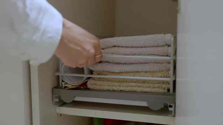 ベージュ色のタオルがグレーのスライディング式下部キャビネット整理棚に整然と置かれたキッチンの空間