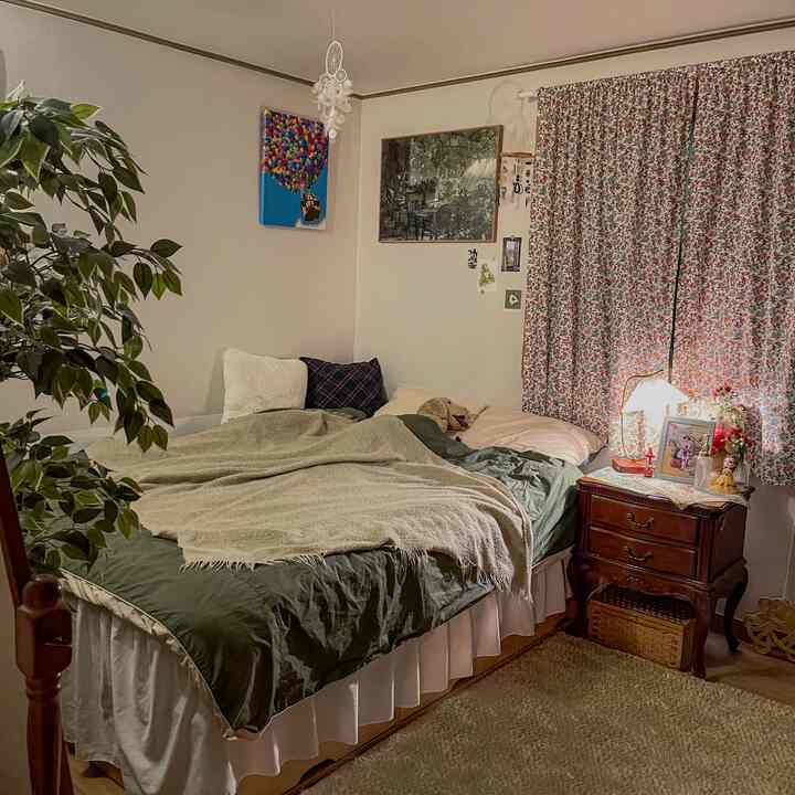 ヴィンテージ感のあるグリーン調の寝室、花柄のカーテンとナイトテーブルが配置された落ち着いた空間