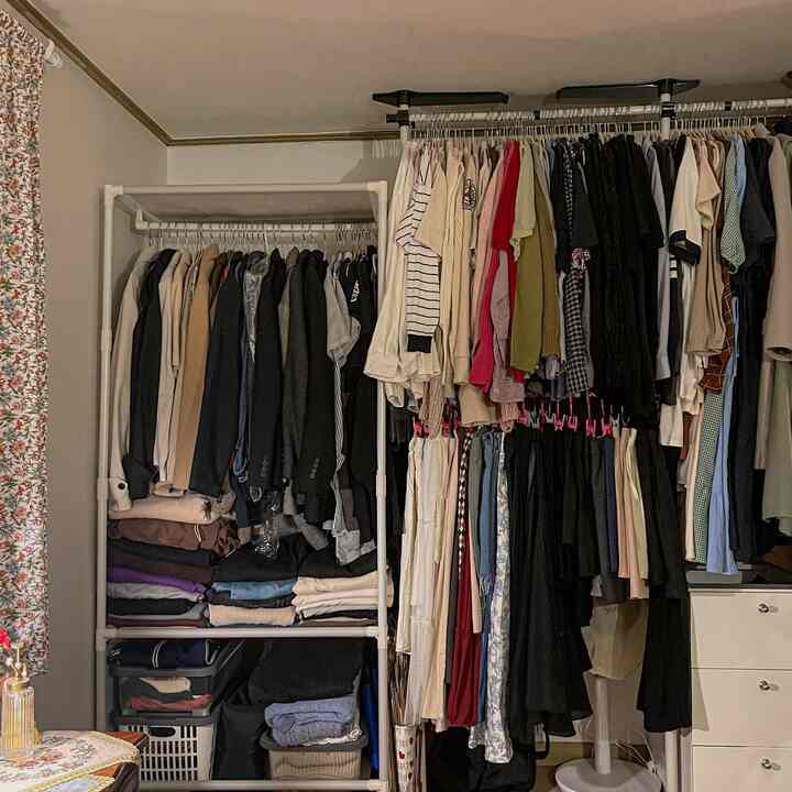 ホワイトとブラウンのトーンのウォークインクローゼット、2つのハンガーラックに整頓された服が配置され、ヴィンテージな花柄カーテンがある雰囲気のある寝室