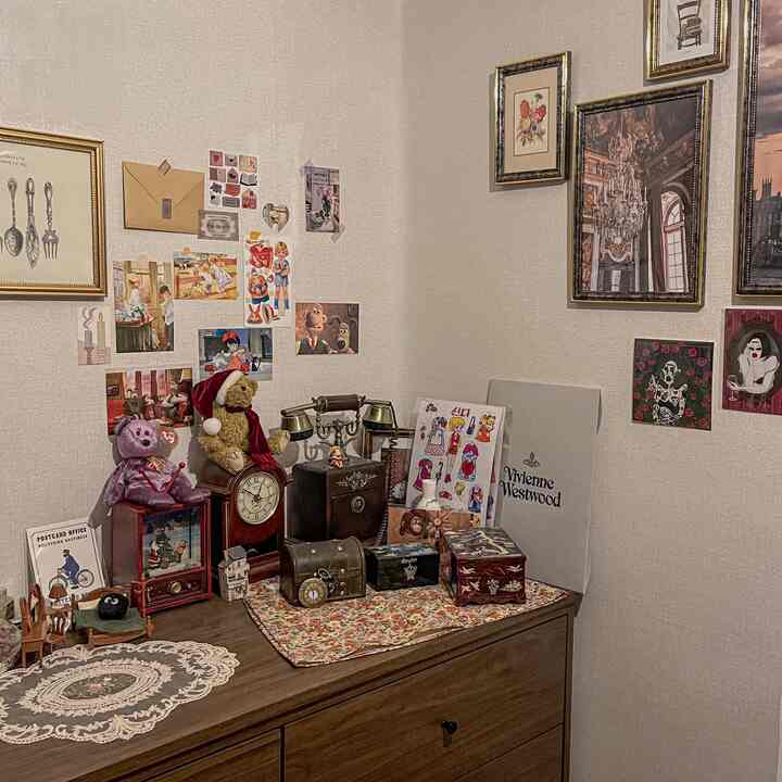 白い壁と茶色の木製ドレッサーの上にヴィンテージのオブジェと花柄のテーブルマットが置かれた雰囲気のあるフレンチカントリースタイルの空間