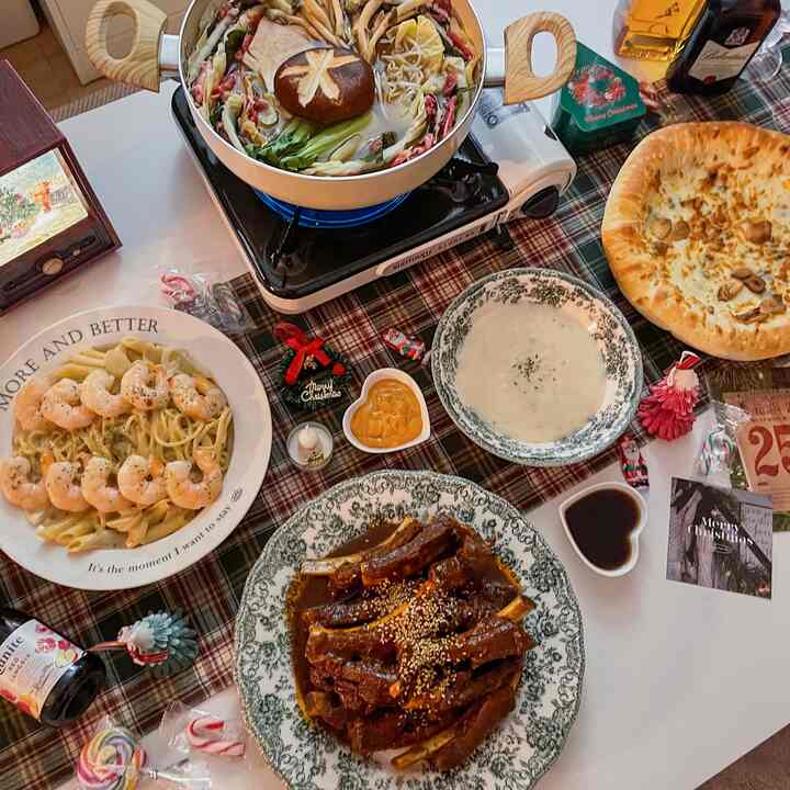 赤のチェック柄テーブルランナーと様々なクリスマス料理が置かれた白いダイニングテーブル、温かく居心地の良いホームパーティー空間