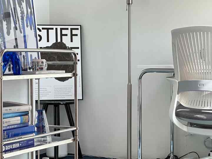 白とグレーのトーンのコンパクトなホームオフィス、金属製トロリーとデスク、オフィスチェアが配置されたすっきりとした作業空間