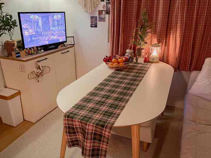 白を基調としたリビング、赤いチェック柄カーテンとテーブルランナー、居心地の良いソファと装飾品が配置された空間