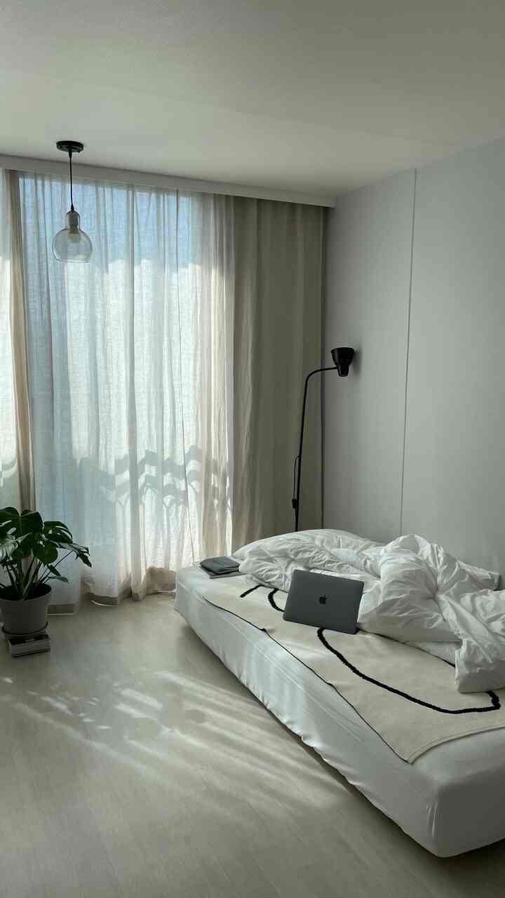 白とベージュの色調の寝室、大きな窓際にベージュのカーテンとベッドが配置されたシンプルで自然なインテリア