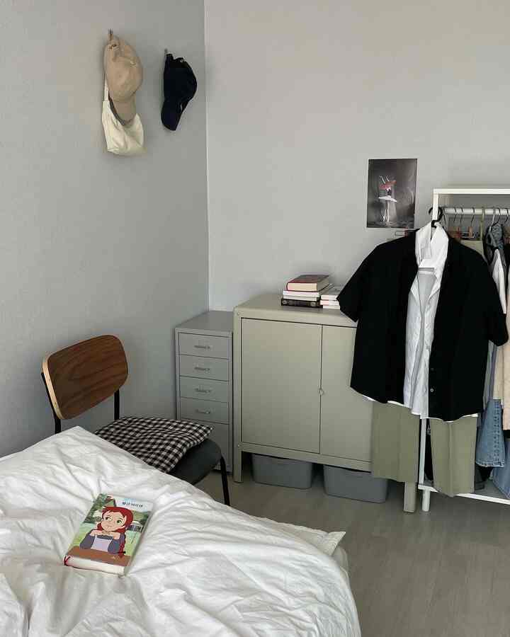 白とグレーのトーンの寝室空間、左にベッド、右に衣類ラックと収納キャビネットが配置された整った部屋