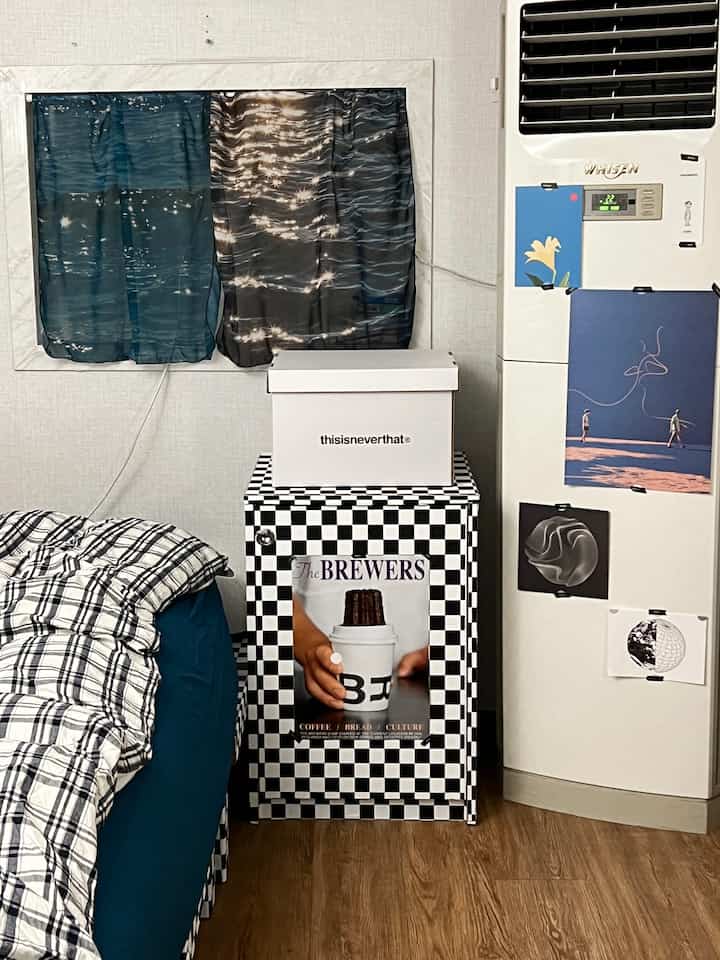 ベージュの壁と床、ブルーの寝具とチェッカー柄の収納が配置された寝室、多様なポスターが飾られたシンプルモダンなインテリア