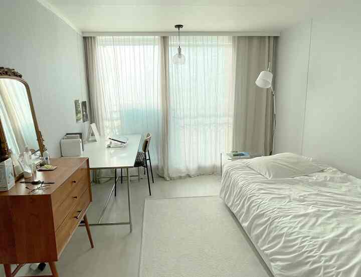 ベージュとホワイトの色調の寝室、ベッドとデスク、柔らかいカーテンが配置された暖かい雰囲気のあるインテリア