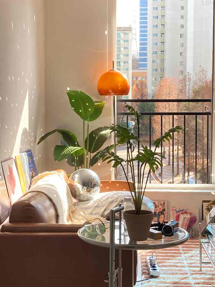 温かみのあるナチュラルなブラウンとオレンジ色調のリビング、窓辺に配置されたソファと植物がある日当たりの良い空間