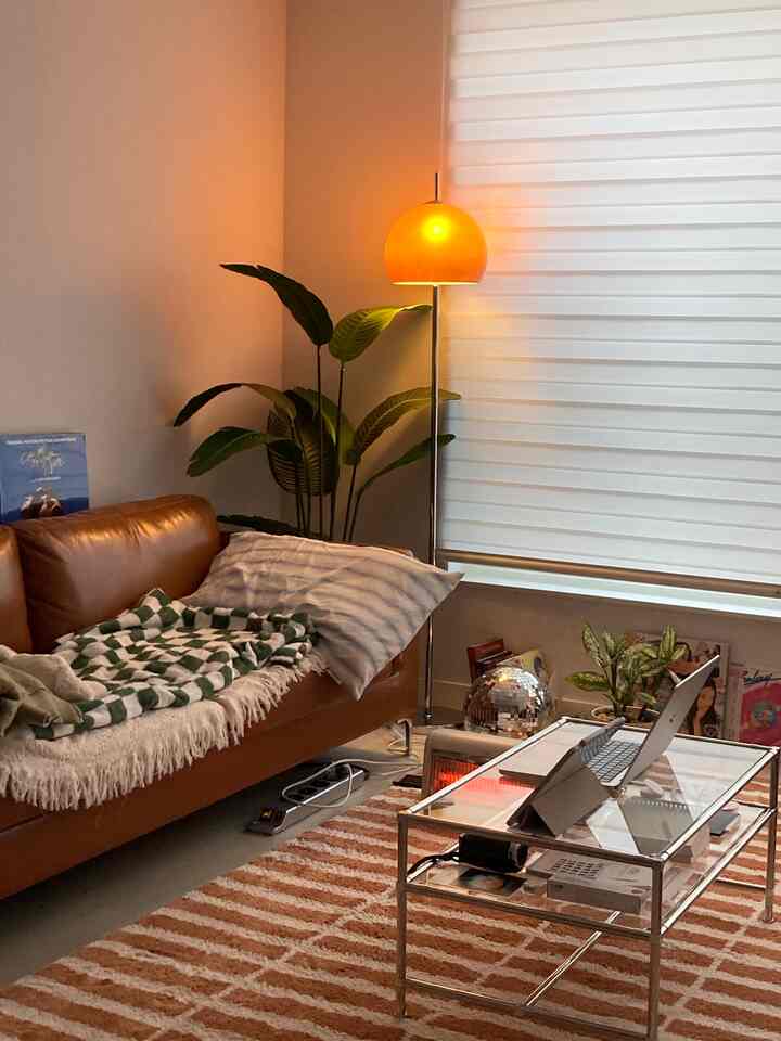 暖かいオレンジとブラウンの色調のリビング、レザーソファ、フロアランプ、植物が配置された雰囲気のある空間