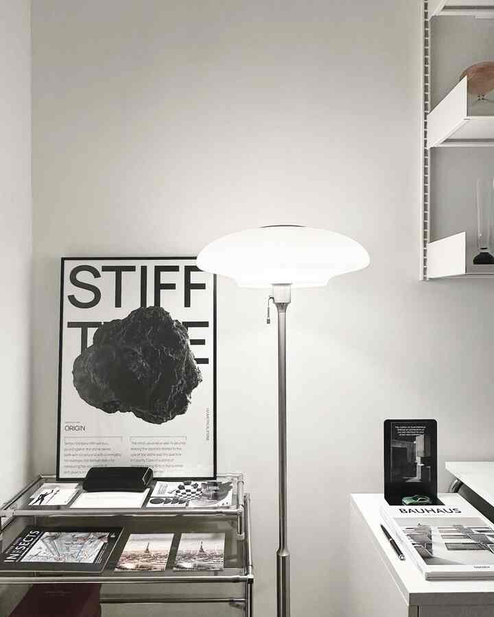 白を基調としたワンルーム、モダンなフロアランプとモノトーンのポスターが配置されたシンプルなインテリア
