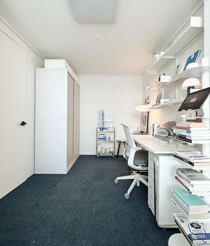 白とネイビーのトーンの小さな書斎、整理された本棚とコンピュータデスクが配置されたシンプルモダンなオフィス空間