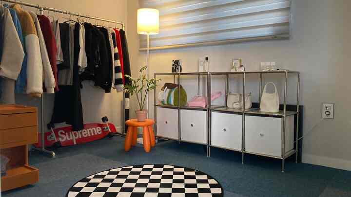 白い壁とスカイブルーの床のコンパクトな部屋、オープンクローゼットと金属製収納が配置された清潔感のあるインテリア