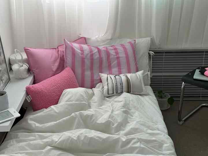 白とピンクの色調の寝室、枕とカーテンが配置された雰囲気のあるインテリア