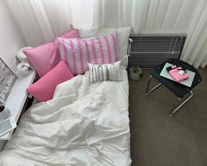 白とピンクの色調の一人寝室、ベッドとクッションが配置された落ち着いた雰囲気のモダンな空間