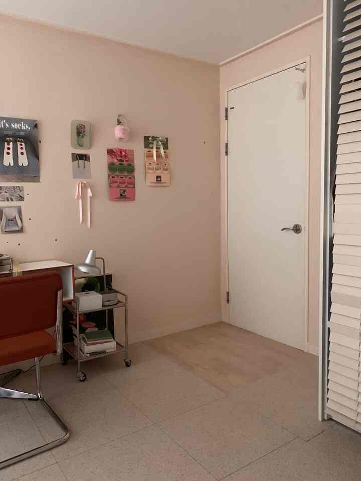 ベージュ色の壁と明るい木製床が特徴のナチュラルでヴィンテージ感のあるホームオフィス、オレンジ色のオフィスチェアとデスクが配置された空間