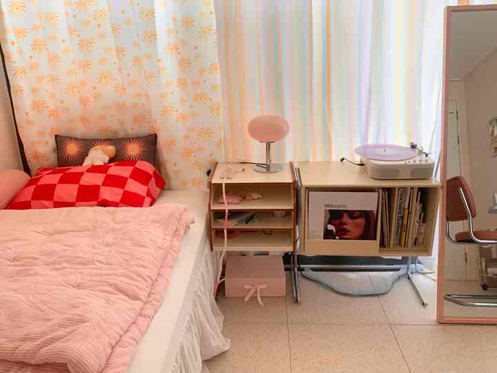 ピンクとホワイトの色調の寝室、ベッドとボヘミアンスタイルのバイニールサイドテーブル、LPターンテーブルが配置された雰囲気のあるインテリア