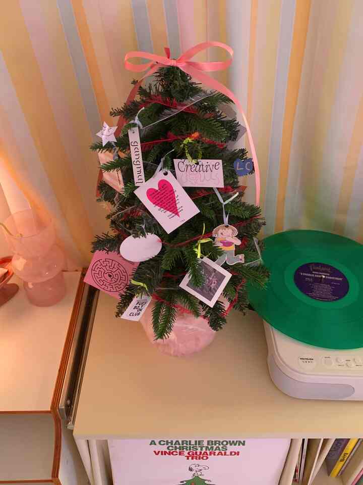 黄色のストライプ壁紙と小さなクリスマスツリーが置かれたサイドテーブル、その隣にグリーンのLPターンテーブルが配された居心地の良い空間