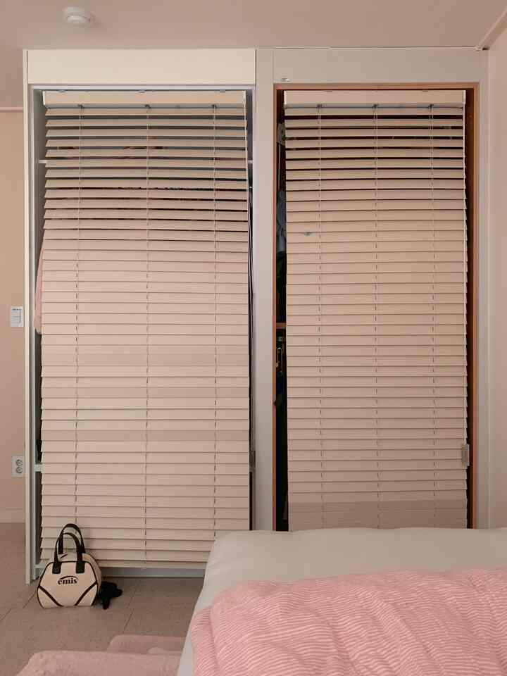 柔らかなベージュとピンクのトーンが調和する寝室、ブラインド付きのクローゼットとベッドが配された温かみのある空間