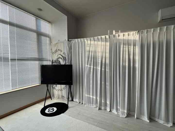 明るいホワイトトーンのリビングルーム、白い大きなカーテンとアルミブラインドが配置されたモダンなインテリア