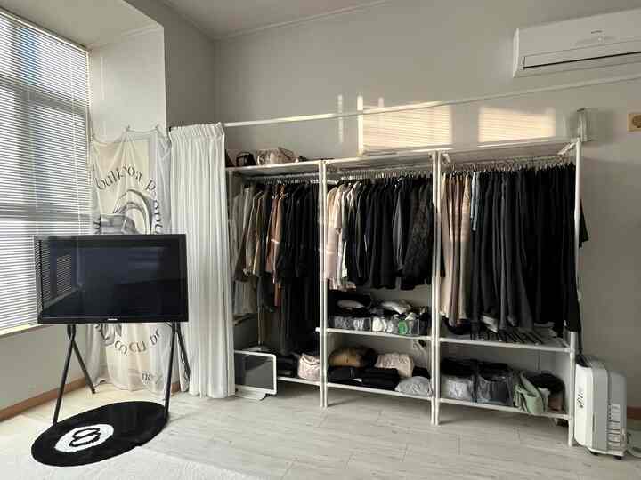 白を基調としたウォークインクローゼット、整頓された無ボルト組立のハンガー、カーテン、ブラインドが配置されたミニマルなインテリア