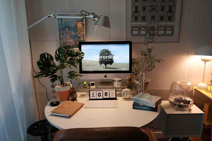 白と茶色のトーンが特徴のコンパクトなホームオフィス、壁照明や植物、デスク上のインテリアが調和する雰囲気のある空間