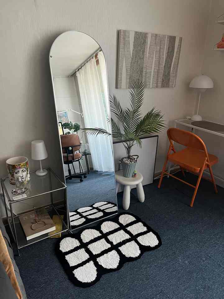 黒と白のトーンのリビング兼ホームオフィス、ミッドセンチュリーモダンスタイルのオレンジの折り畳み椅子と大きな全身鏡が配置された雰囲気のあるインテリア