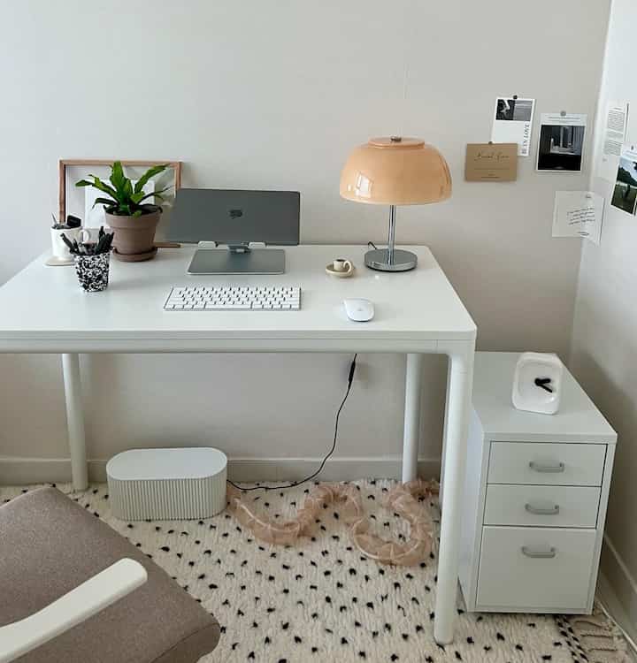 白とベージュのトーンのホームオフィス、シンプルなデスクとテーブルランプ、植物が配置された落ち着いた雰囲気の空間